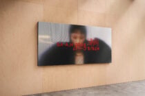 Wide black display screen mounted horizontally on neutral wood interior wall