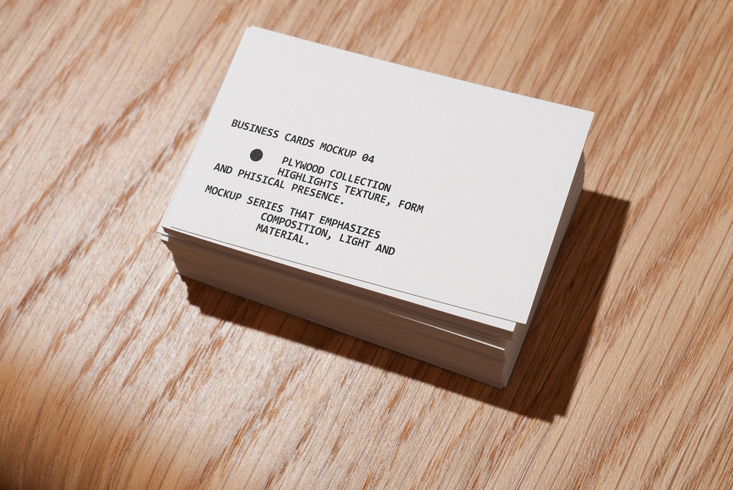 Stacked white business cards on light wood with natural shadow
