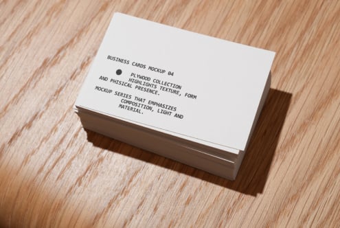 Stacked white business cards on light wood with natural shadow
