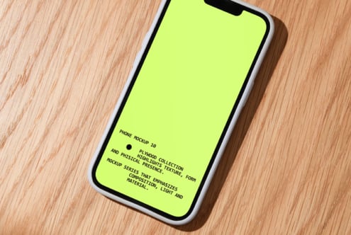 iPhone mockup on wood table with neon yellow screen, shot from above angle