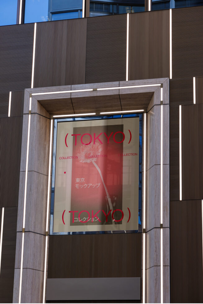 Concrete storefront with red Tokyo Collection poster displayed on illuminated glass window
