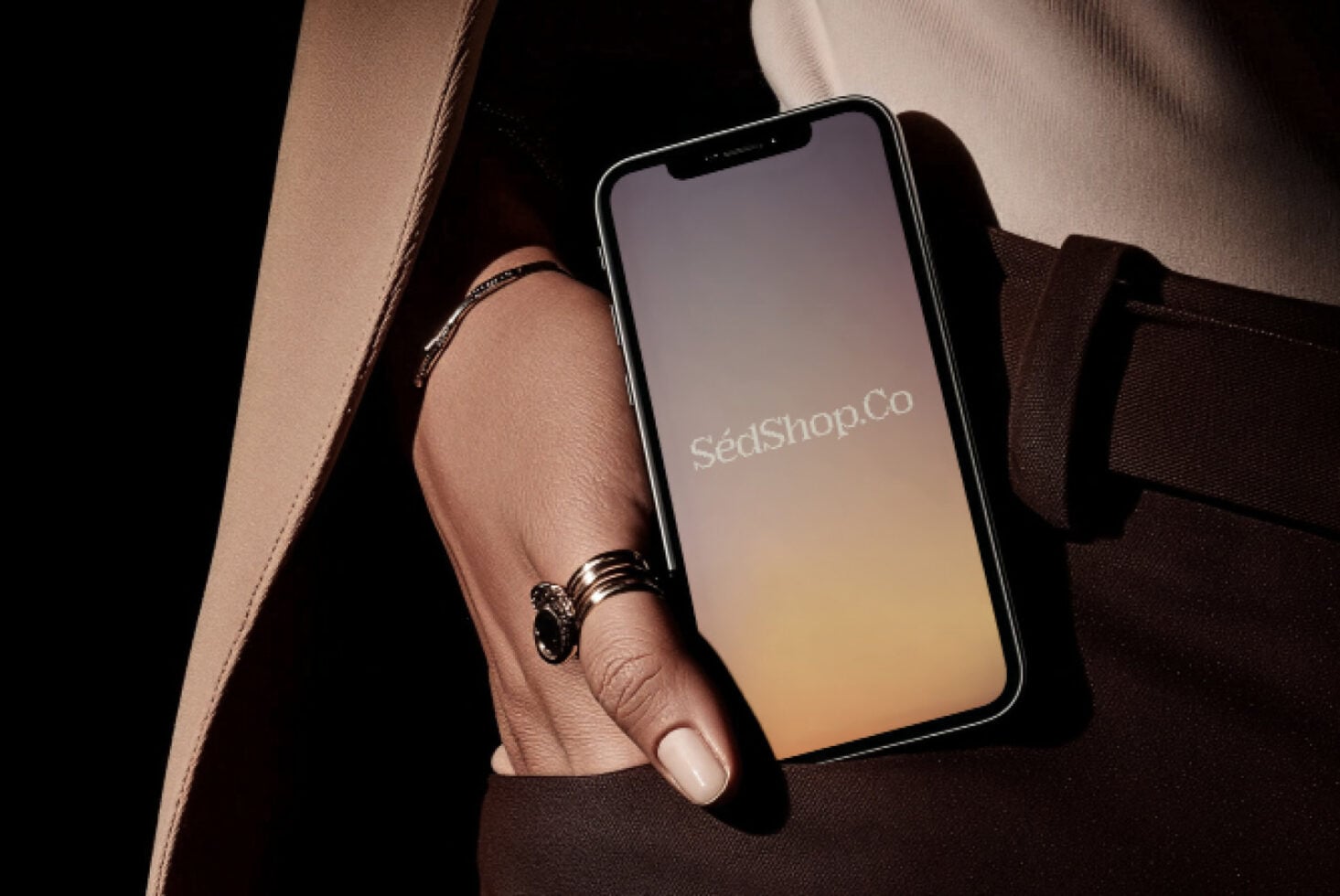 iPhone held by manicured hand showing peachy gradient display with SédShop.Co branding