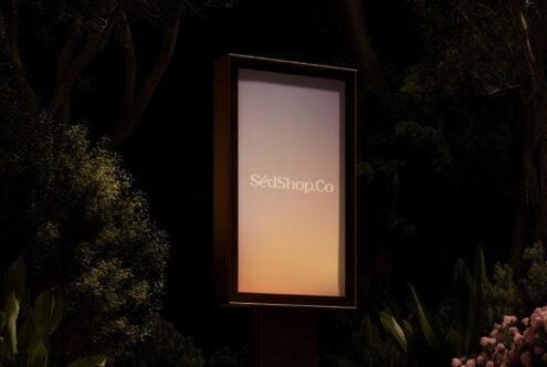 Glowing vertical billboard in forest setting at night displaying SédShop.Co branding