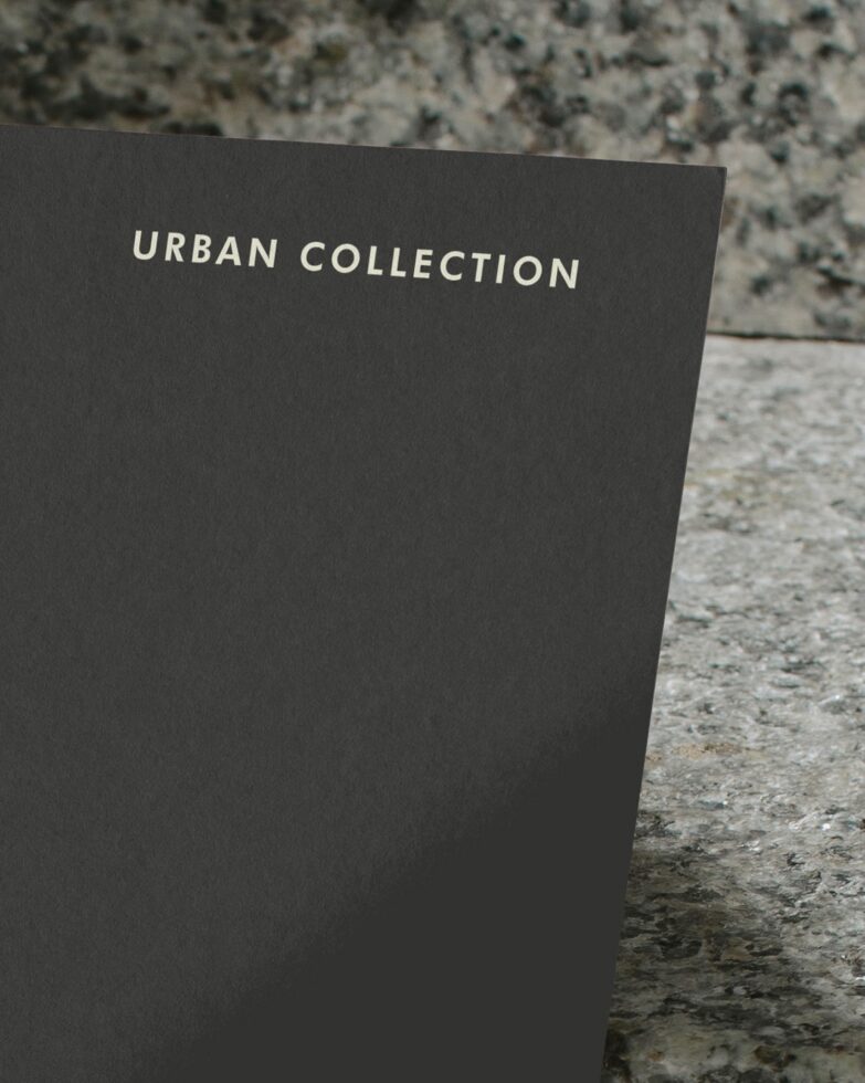 Close up of charcoal card leaning against rough concrete with Urban Collection text