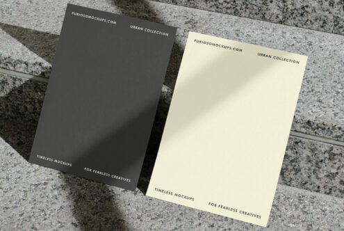 Dark gray plus cream colored cards angled on speckled stone background with shadows