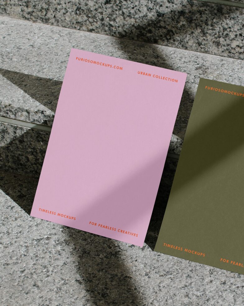 Pink folder with orange text next to olive green folder on concrete surface