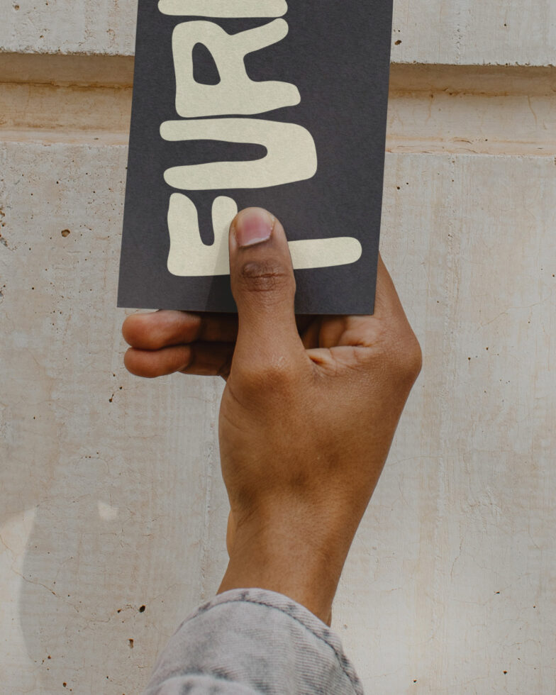 Black vertical card held up showing cream text on concrete wall