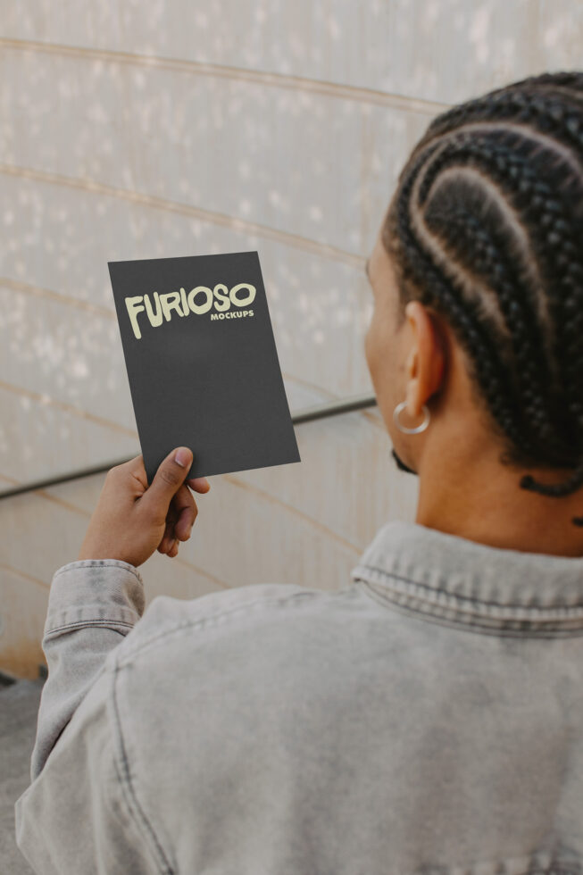 Black business card mockup held up by person wearing gray sweatshirt