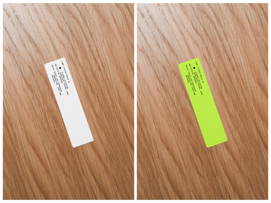 Narrow white plus neon yellow label stickers on wooden surface showing front back views