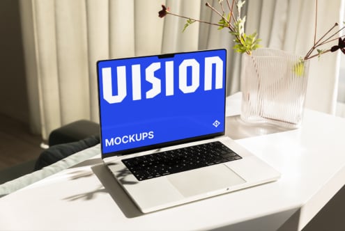 Laptop screen displaying VISION MOCKUPS in bright blue, modern workspace with plants