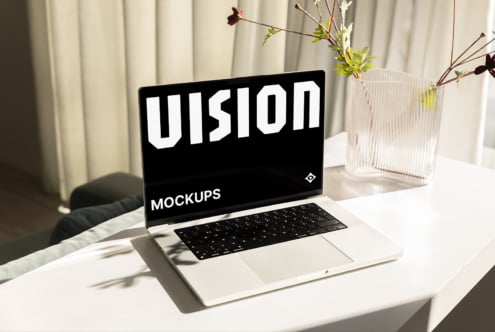Laptop screen showing VISION MOCKUPS text on white background, minimal desk setup