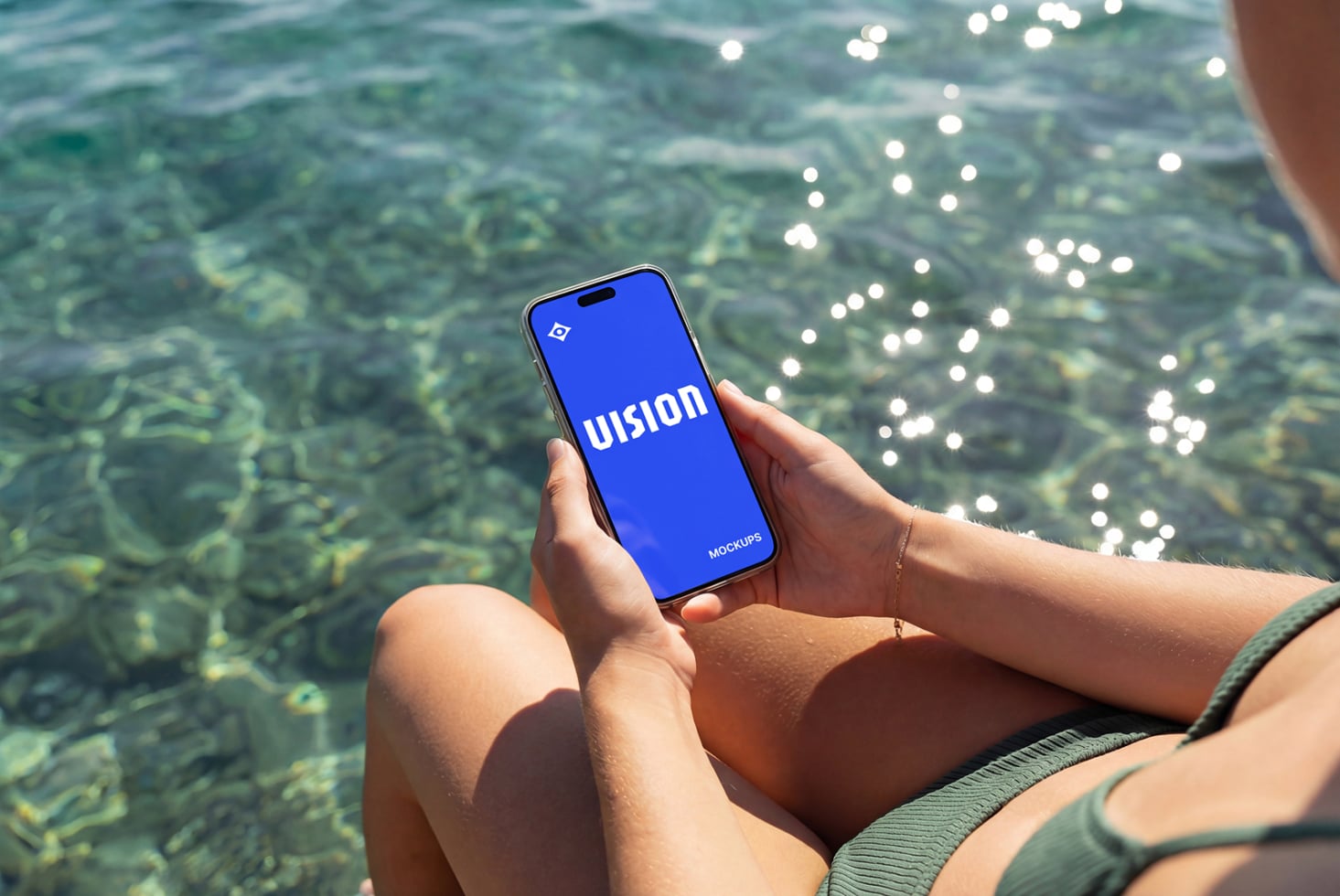 Phone displaying blue screen held over turquoise ocean water with sunlight glinting