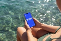 Phone displaying blue screen held over turquoise ocean water with sunlight glinting