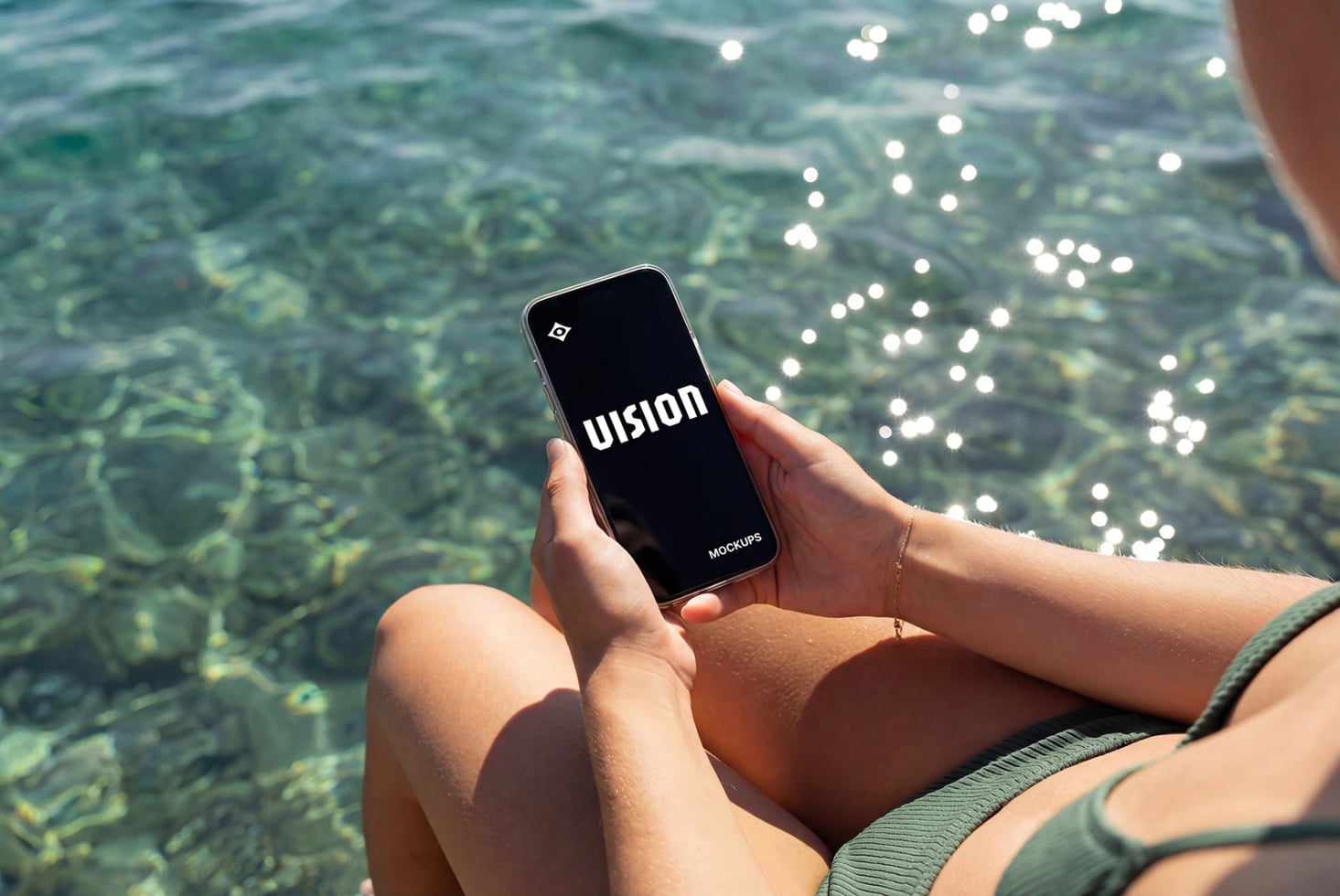 Phone held in hands above clear ocean water with sunlight reflections