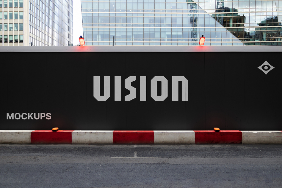 Black hoarding with VISION in gray letters, red warning barriers, urban skyline