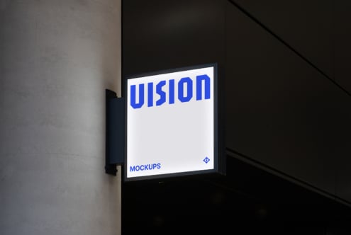 Illuminated storefront sign mounted on dark wall showing white VISION text on light background