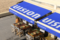 Bright blue retro awning mockup stretched over outdoor café seating with wooden tables