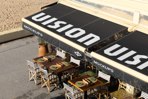 Overhead shot of storefront awning with black canopy displaying large white text, cream-colored frame, dining tables below with striped chairs