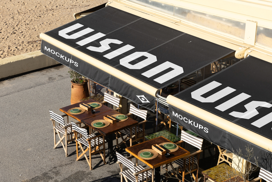 Overhead shot of storefront awning with black canopy displaying large white text, cream-colored frame, dining tables below with striped chairs