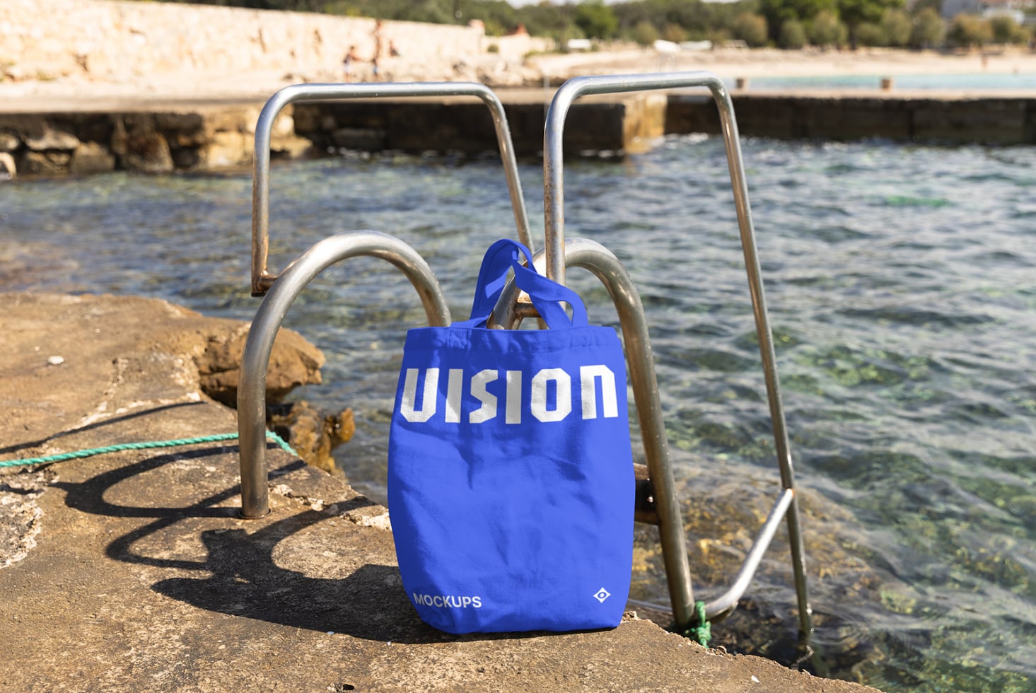 Bright blue canvas tote bag hanging on metal railing overlooking coastal water