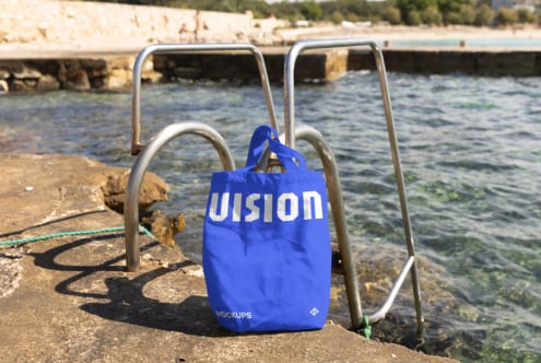 Bright blue canvas tote bag hanging on metal railing overlooking coastal water