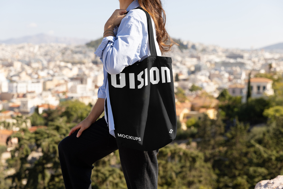 Black tote bag with VISION text worn over shoulder overlooking city landscape