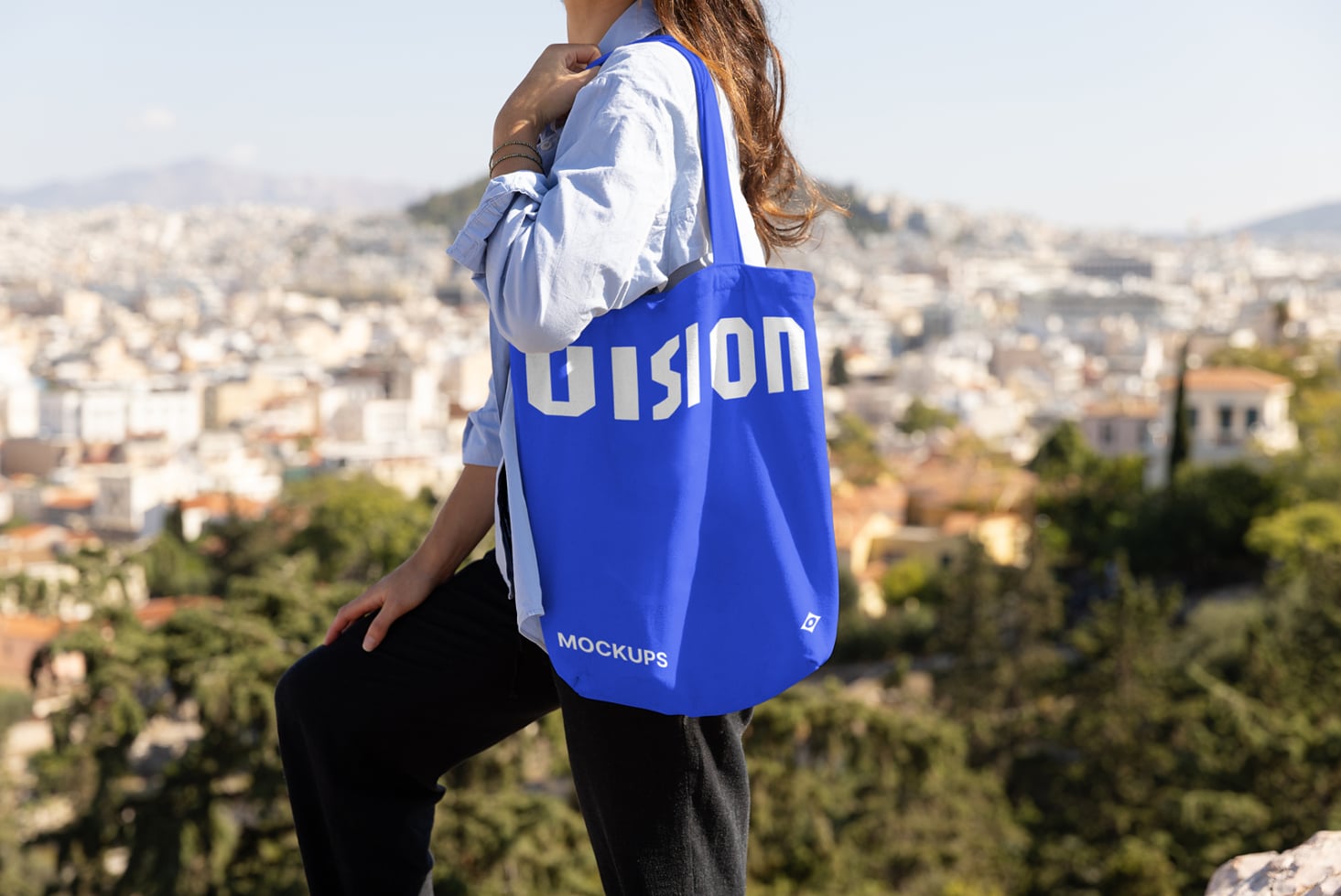 Woman wearing blue tote bag overlooking cityscape from hilltop viewpoint