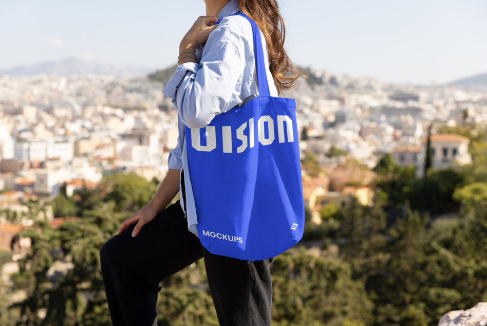 Woman wearing blue tote bag overlooking cityscape from hilltop viewpoint