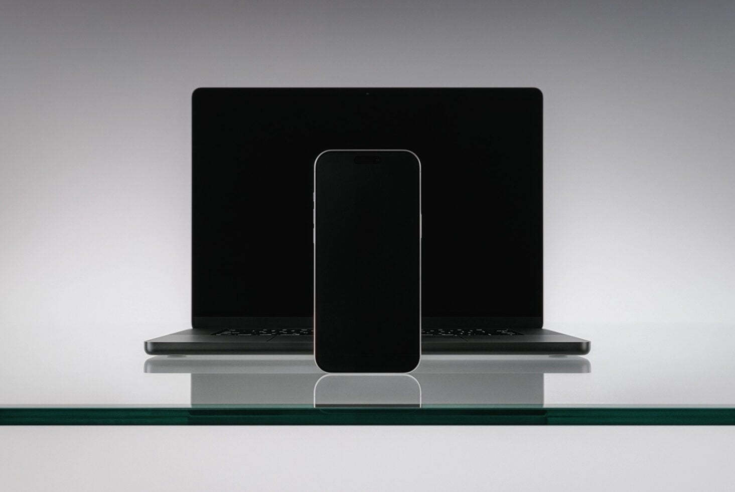 Blank phone screen positioned in front of open laptop on glass