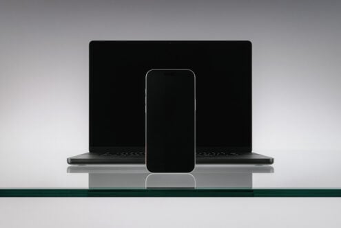 Blank phone screen positioned in front of open laptop on glass