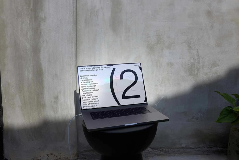 Laptop mockup showing clean web layout with bold number 2 on concrete wall backdrop