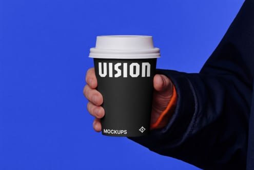 Hand holding black coffee cup with white VISION text against blue background