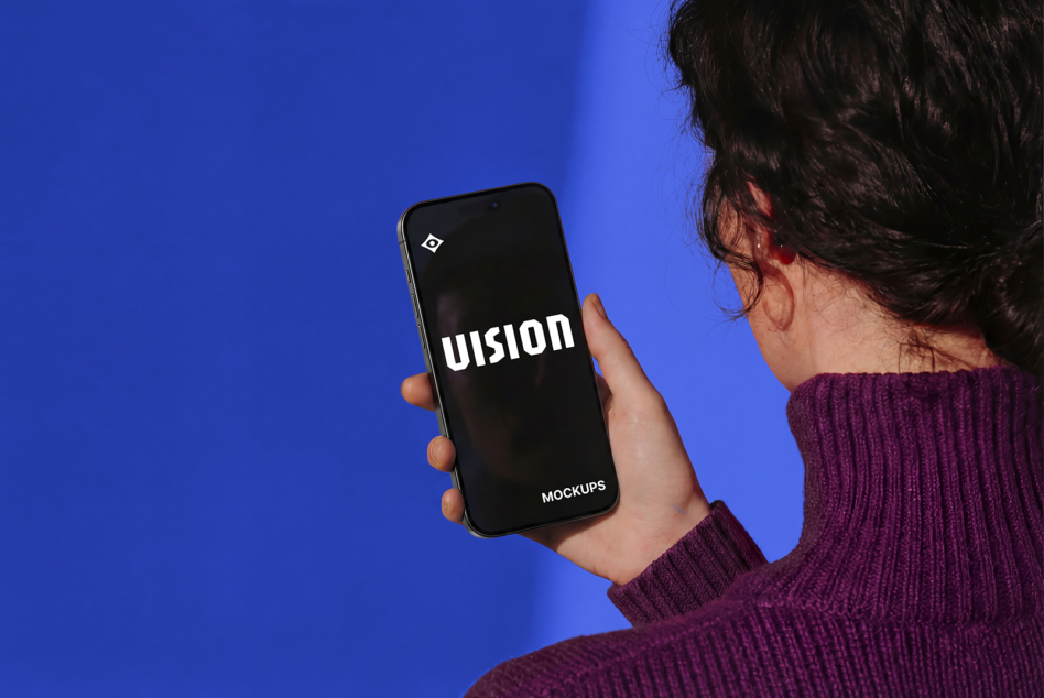 Person in burgundy sweater holding iPhone with VISION text on blue background