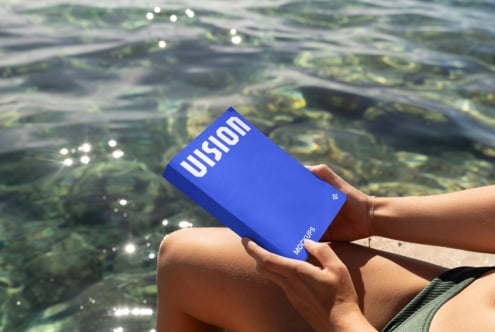 Bright blue box mockup held over sparkling ocean water with white VISION text visible