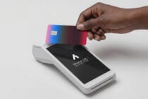 Hand holding gradient pink credit card over white payment terminal with logo