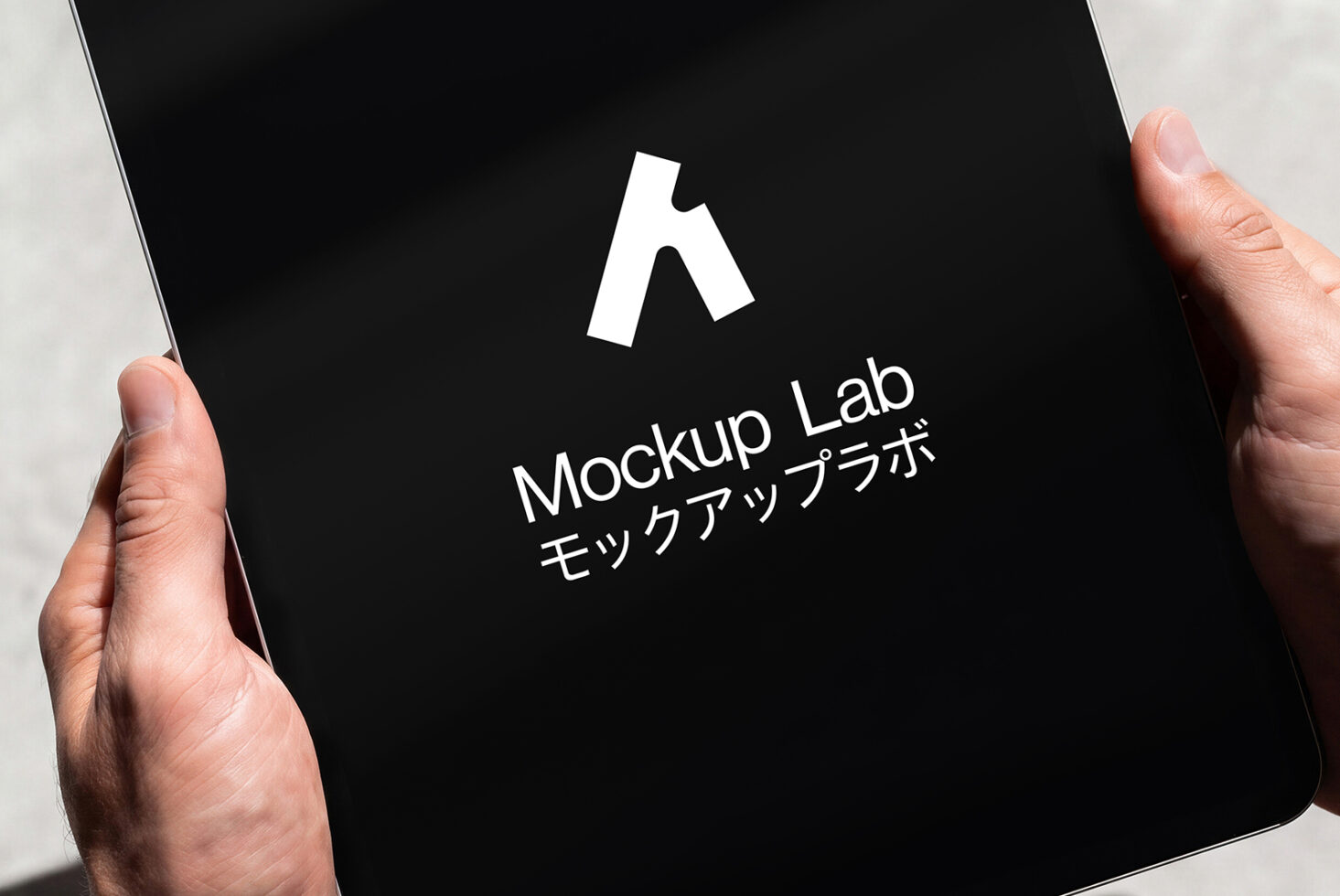 Hands holding tablet showing Mockup Lab logo on black screen