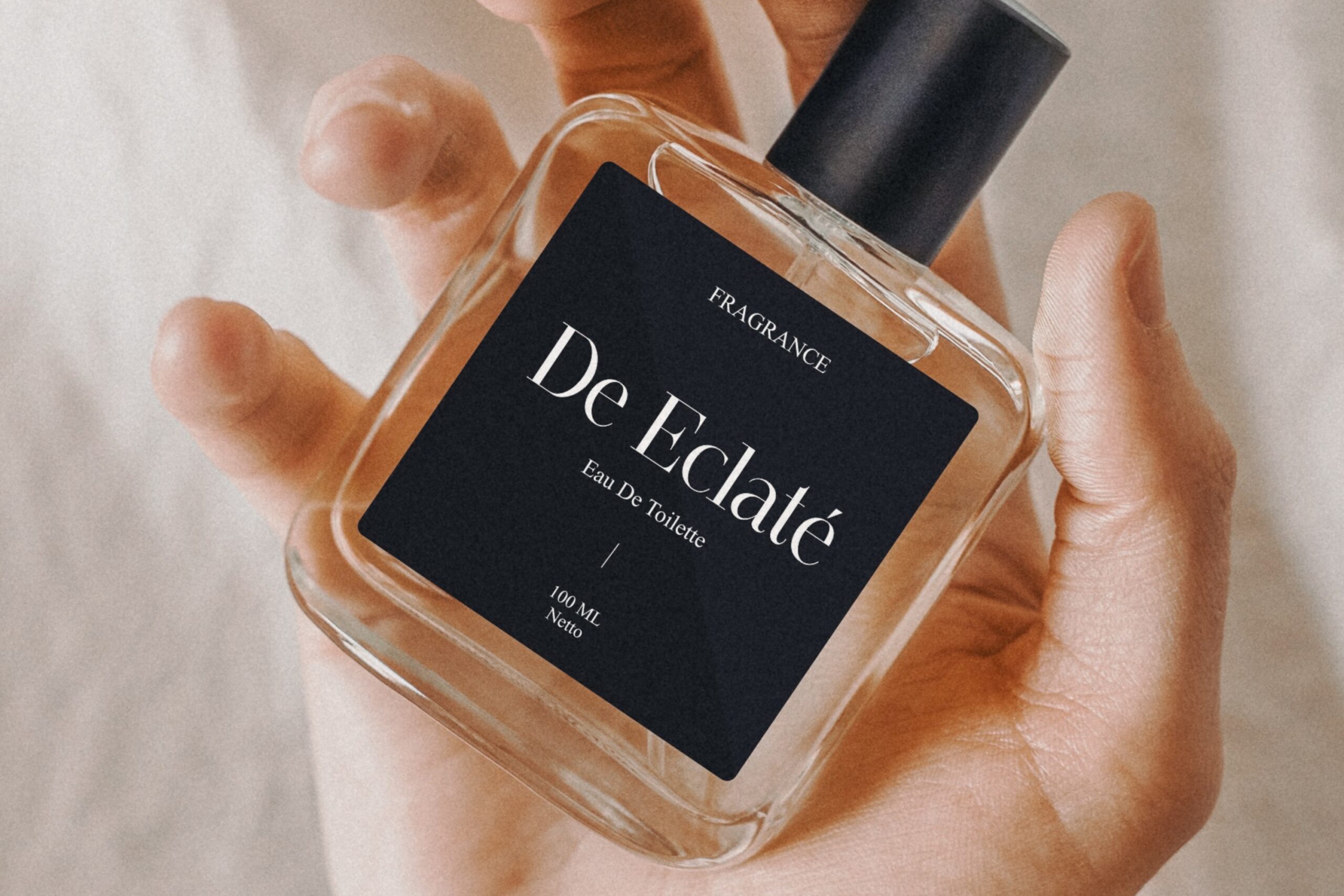 Hand holding clear glass fragrance bottle with black De L'Eclate label