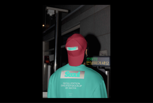 Mockup of a person in a teal sweater with Seoul graphic and red cap in an urban setting. Ideal for designers seeking trendy apparel graphics.