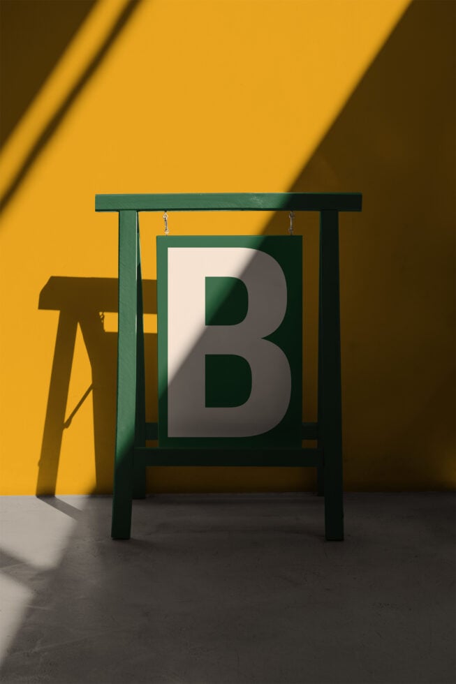 Green wooden sign stand with cream card displaying large silver B letter