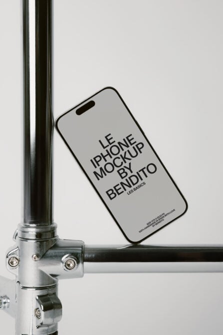 iPhone leaning against metal pole with light gray screen showing mockup text