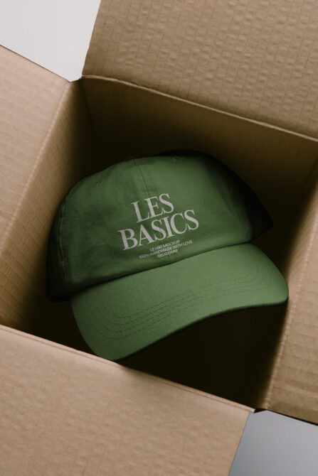 Sage green embroidered caps layered in open brown shipping box, overhead shot