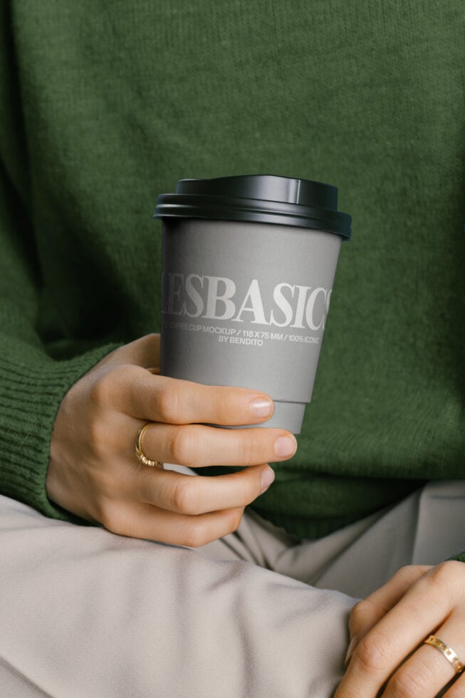 Hand holding coffee cup mockup wearing green sweater against green backdrop