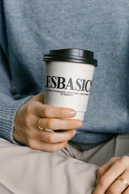 Hand holding coffee cup mockup wearing blue sweater against blue textile