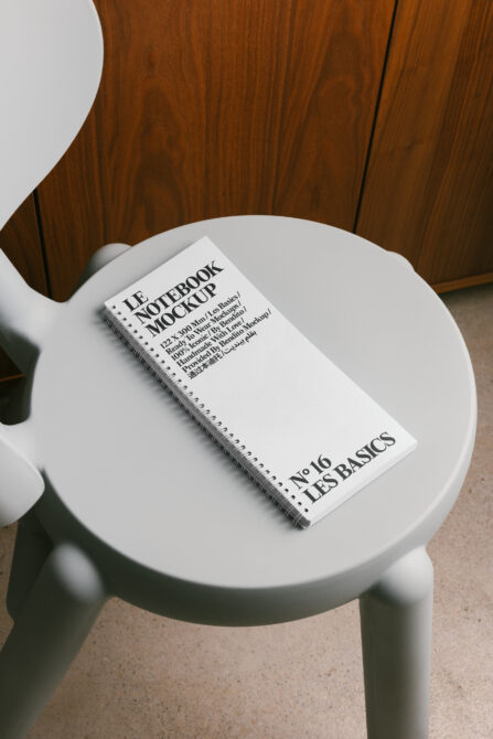 White spiral notebook mockup on light gray round table next to wooden furniture