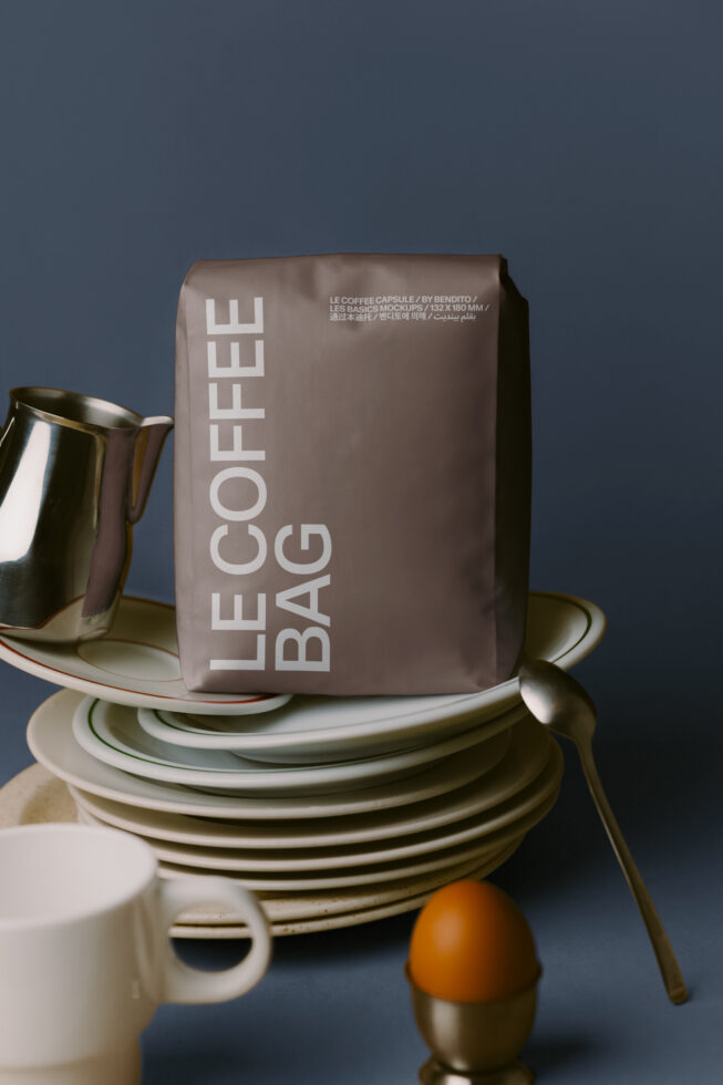 Styled tabletop with stacked white plates, metal pitcher, coffee bag mockup on blue background