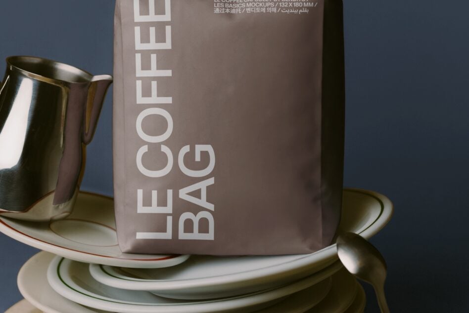 Styled tabletop with stacked white plates, metal pitcher, taupe coffee bag mockup on blue background
