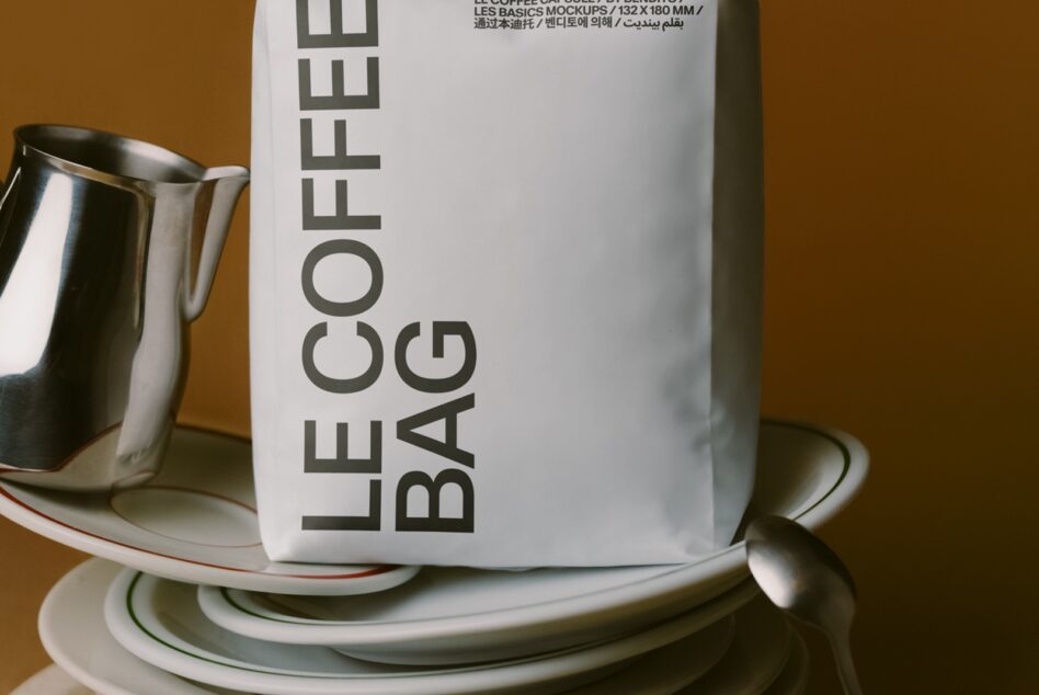 White mug with vertical Le Coffee Bag text on warm brown background next to metal pitcher