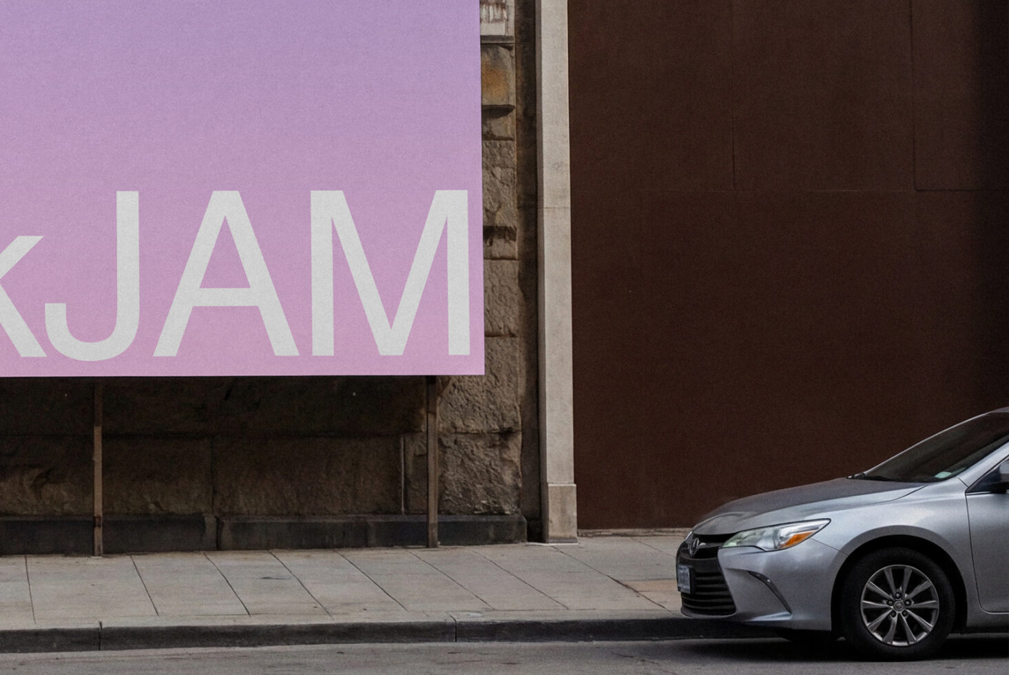 Silver car parked in front of pink storefront wall with large white JAM lettering visible