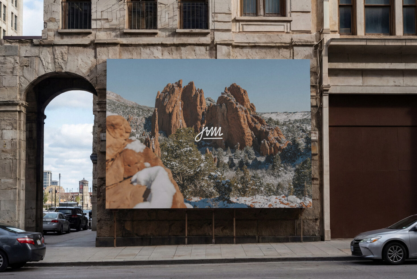 Outdoor billboard on stone building displaying red rock mountains with handwritten jam script overlay