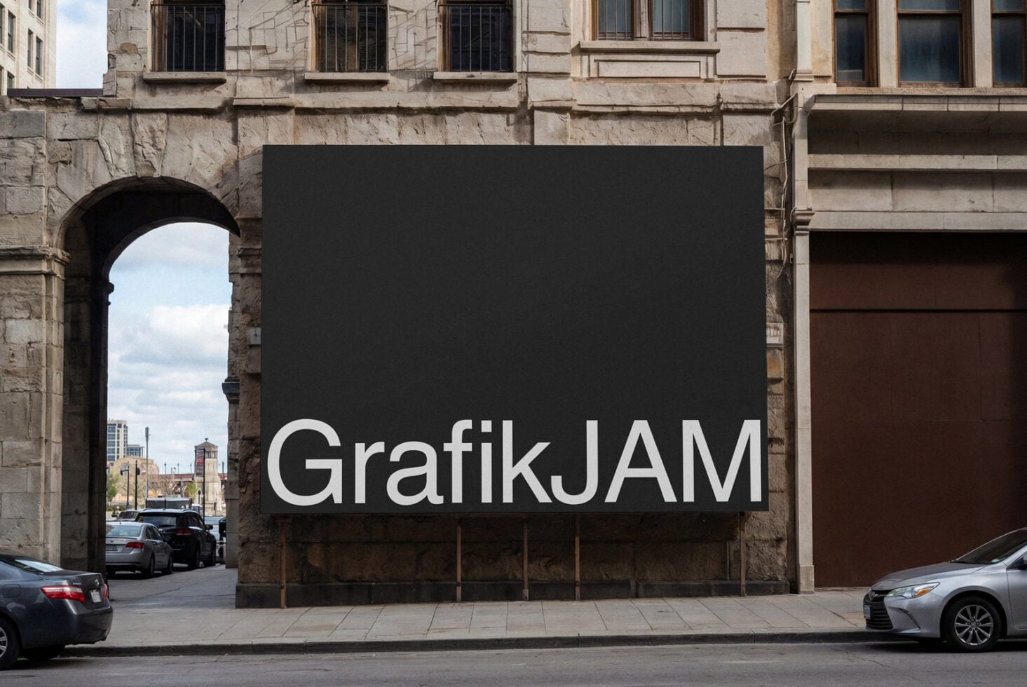 Dark billboard on stone facade displaying bold GrafikJAM wordmark in clean sans serif font